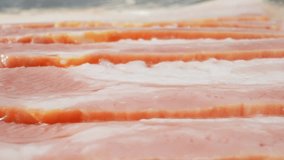 Mesmerizing macro video showcases raw bacon glistening with marbled fat, awaiting sizzling heat. A tantalizing glimpse into the delicious potential of this savory delight. Bacon background. 4K
