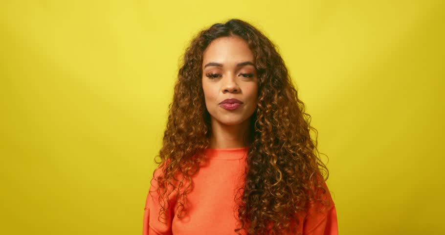 Young multiracial woman pulls silly face with fingers making eyeglasses, yellow