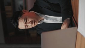 Appalled entrepreneur getting stressed when finding expensive mistake in accounts on laptop in workplace. Vertical video of asian employee understanding negative impact on company's future success.