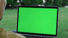 Young Man Using Laptop With Green Mock-up Screen Outside in City Park. Close-up of Green Laptop Screen