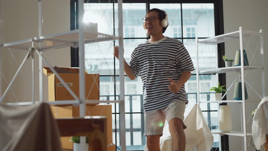 greeting happiness joyful asian adult male wearing casual cloth and wirreless headphone dance music lover while unpack stuff relax from home moving house relocation ,he is happy to move in new house