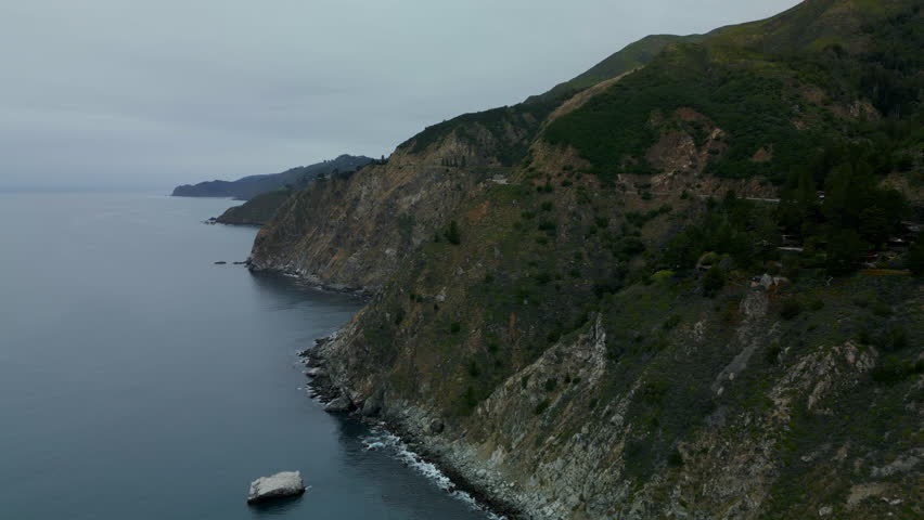 Aerial drone view of Pacific Coast Highway ocean cliffs with waves crashing on shore near Big Sur, Monterey California