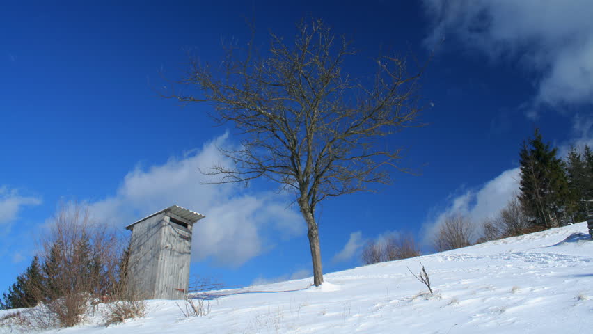 Time-lapse of white clouds passing by over winter landscape with outhouse in Carpathian Mountains