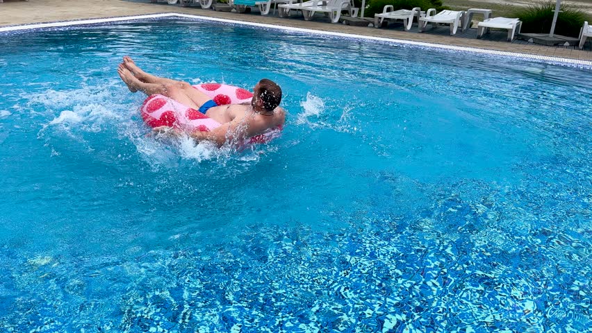 Happy adult man swimming in an outdoor summer pool on a red inflatable swim ring.