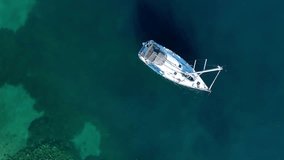 Aerial top down view, a anchored sailboat off the coast of an island. Beautiful calm sea water with one yacht on the sea in Sunny day. Sailing boat. Yachting video. Sailboat from drone. Sailing video
