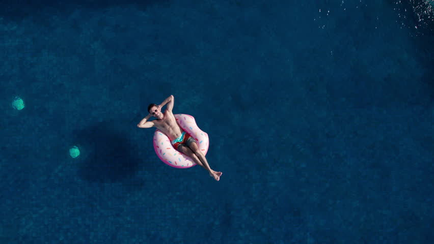 Aerial top view of athletic man swim with inflatable mattress donut in infinity pool on luxury private villa. Concept of rich life, relax rest on summer vacation, take sunbathing enjoy,  | Shutterstock HD Video #1106632505