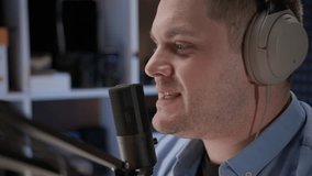 Close up radio host sit in studio and communicates with audience. man in blue shirt and headphones sits in recording studio in front of professional microphone. announcer reads text for video. 