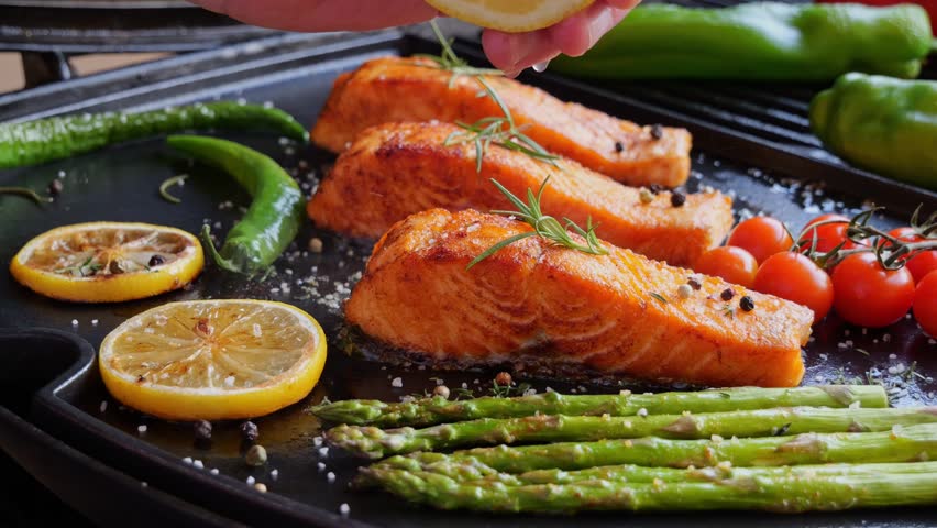 grilling fillet salmon with asparagus, tomato, lemon. A chef's hand is squeezing a fresh lemon over a peace of red sea fish. Cooking process. Slow motion. close up Royalty-Free Stock Footage #1106634951
