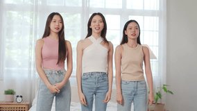 Group of young Asian Chinese female friends dancing in front of a mobile phone to share on social media application in bedroom. Cheerful Korean women influencer having live streaming on smartphone.
