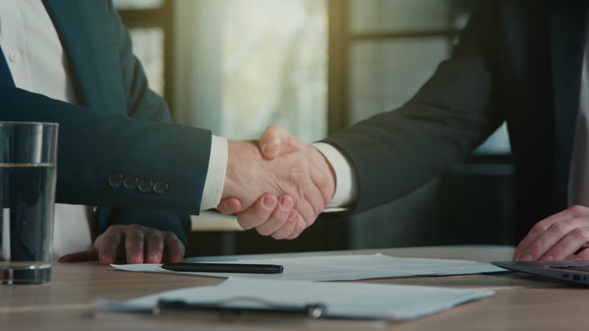 Close-up unrecognizable men businessmen business partners sign contract agreement successful transaction deal handshake shake hands in office sunlight sun rays signing document corporate partnership