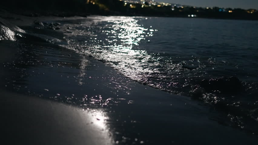 Close-up Mediterranean sea waves in moonlight in darkness. Closeup ocean water rolling on beach at night outdoors