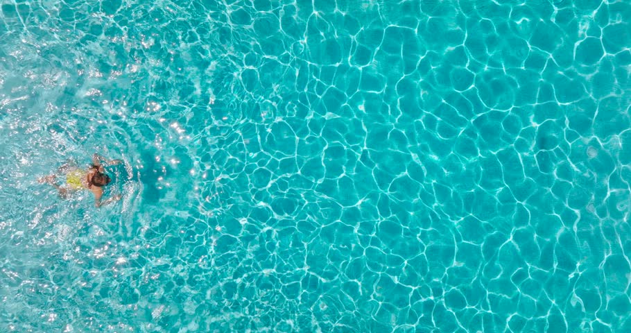 Aerial view of a woman in yellow swimsuit swimming in the pool. Summer lifestyle