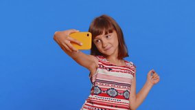 Young school girl blogger influencer taking selfie on smartphone, communicating video call online with subscribers in social media app. Preteen Caucasian child kid isolated on studio blue background