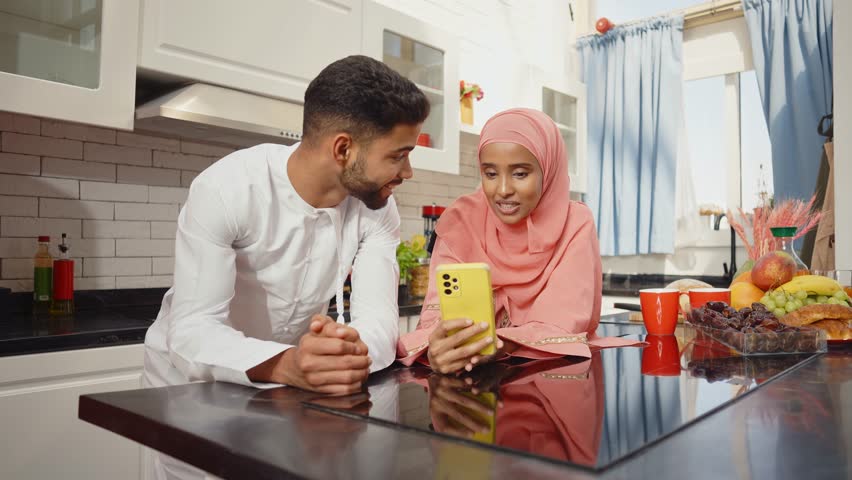 Happy couple wearing traditional outfits from the emirates spending  time in the kitchen of their beautiful modern apartment in Dubai