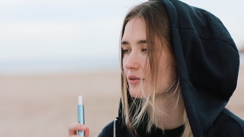 Electronic cigarette technology. Young woman smokes and releases steam from hybrid cigarette device that uses real tobacco refills with a heating pad, tobacco heating system. Bad unhealthy habit. Royalty-Free Stock Footage #1106652225