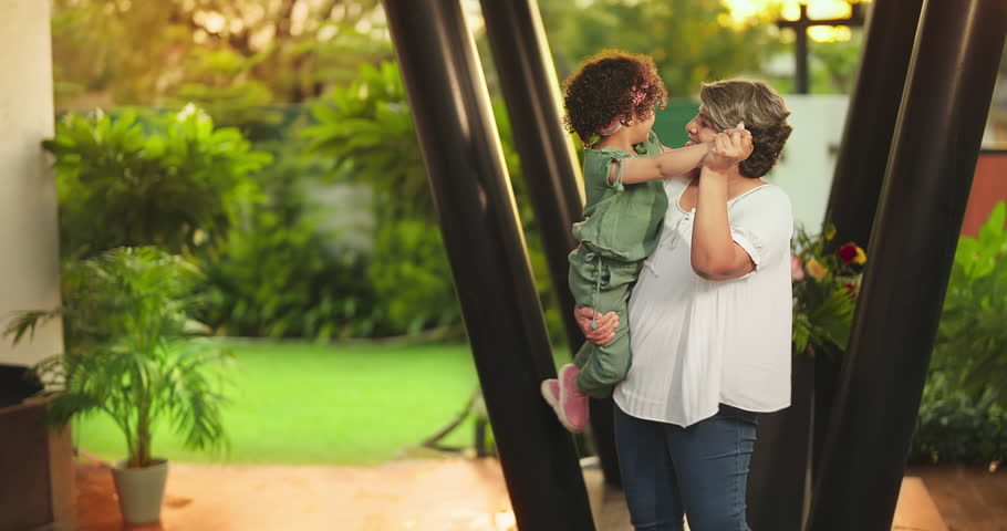 Happy Indian old grandmother holding cute little child girl in arms hands whirl dancing together outdoor home. Beautiful smiling woman sing song spinning small kid daughter enjoying summer holiday