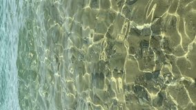 Vertical 4k video of calm blue mediterranean sea or ocean with small soft waves. Close up of pure water surface, sea sandy bottom with stones, happy summer vacation. Sun beam in transparent water.