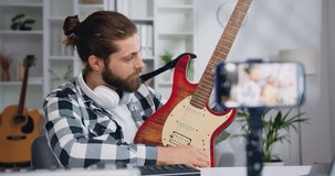 Male teacher blogger recording video class tutorial for play electric guitar on modern smartphone at home studio. Man showing how play for electric giutary for internet auditory