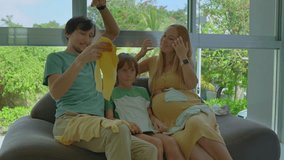 A heartwarming stock video showing a loving family of a father, son, and pregnant mother sitting on a cozy couch, joyfully browsing through adorable tiny clothes for their soon-to-arrive little one