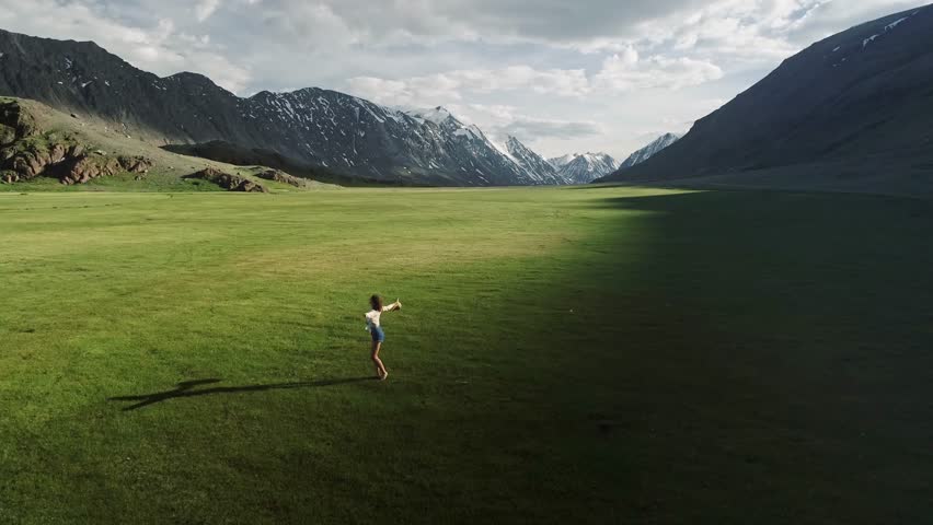 Happy young girl spinning around herself on the field. Mountains and sky are in the background. Cheerful young woman running with hands stretched wide, feeling happy being in connection with nature Royalty-Free Stock Footage #1106668179