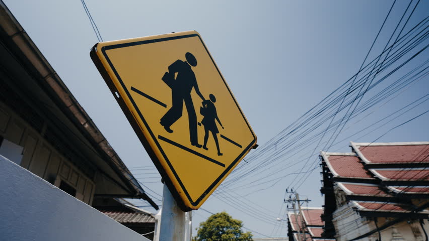 Caution school zone yellow road sign with symbol of parent and child togeather in city district. Dolly moving camera shot Royalty-Free Stock Footage #1106668945
