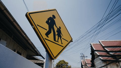 Caution school zone yellow road sign with symbol of parent and child togeather in city district. Dolly moving camera shot – Video có sẵn