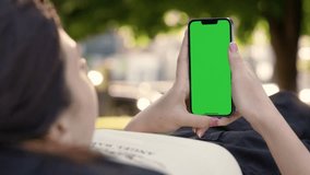 Young Girl Using Phone With Green Mock-up Screen Outside in City Park. Woman Watching Videos, Browsing News and Social Networks in Smartphone 