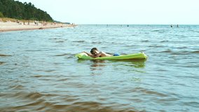 A child floats on a mattress in the sea. The child pushes the mattress with his hand to swim. Soft selective focus. Video clips.