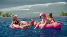 Diverse group of young friends having fun in infinity resort pool with pink inflatable flamingo. Cool party with water splashing and swimming, chilling with the ocean beach view - Powered by Shutterstock - Get 15% off with code: PIKWIZARD15