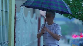 Senior man arriving home during rainy day, holding umbrella and opening gate. Elderly person daily walking routine while raining, slow-motion clip