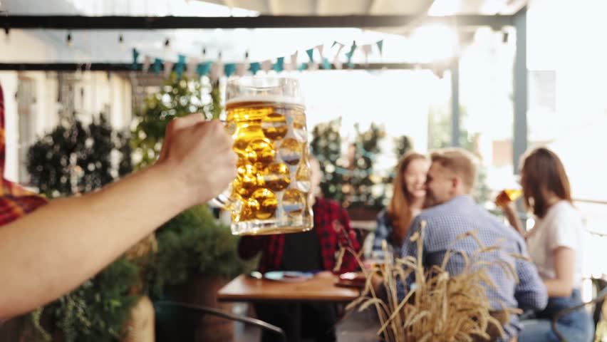 Cheerful young people, friends meeting a pub on warm summer day, drinking delicious lager beer, having good time. Concept of oktoberfest, traditional taste, friendship, leisure time, enjoyment Royalty-Free Stock Footage #1106679395