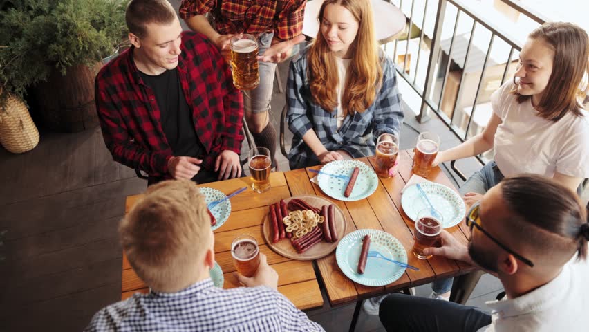 Top view of cheerful young people, friends meeting at cafe, pub, spending time together, drinking beer with sausages and snacks. Concept pktoberfest, traditional taste, friendship, leisure time, joy