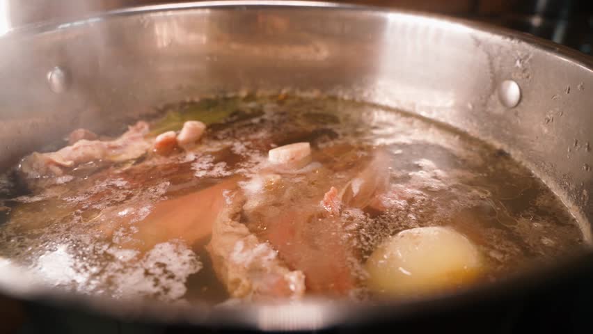 Broth with meat and onions is slowly cooked close-up. Hearty meat broth in a large steaming pot