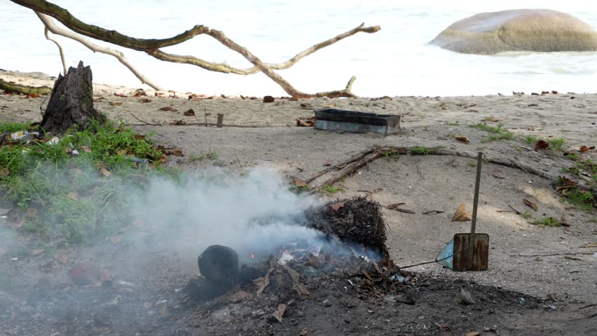 Slow motion open burn rubbish on a sandy beach with smoke billowing