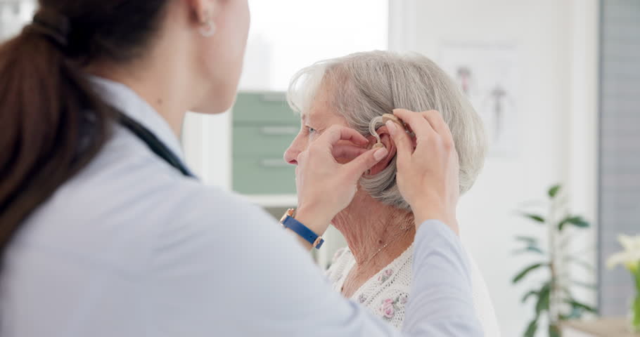 Female doctor, consultation and hearing aid on senior person at clinic for help with problem. Hearing, loss and deaf and installation for elderly woman at appointment with medical professional. Royalty-Free Stock Footage #1106684143