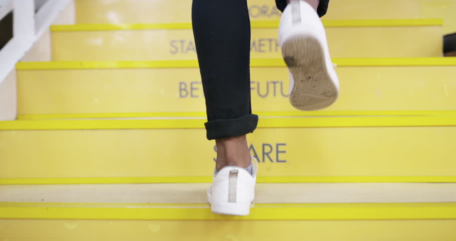 Feet, office stairs and closeup for person with words for motivation, inspiration and signage on steps. Shoes, sneakers and walking at startup with employee, staircase and quote in creative workplace