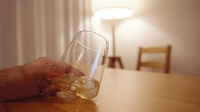 A lone woman twirls a glass of whiskey in her hand, seated behind a wooden table, with warm light softly emanating from a lamp behind her. - Powered by Shutterstock - Get 15% off with code: PIKWIZARD15