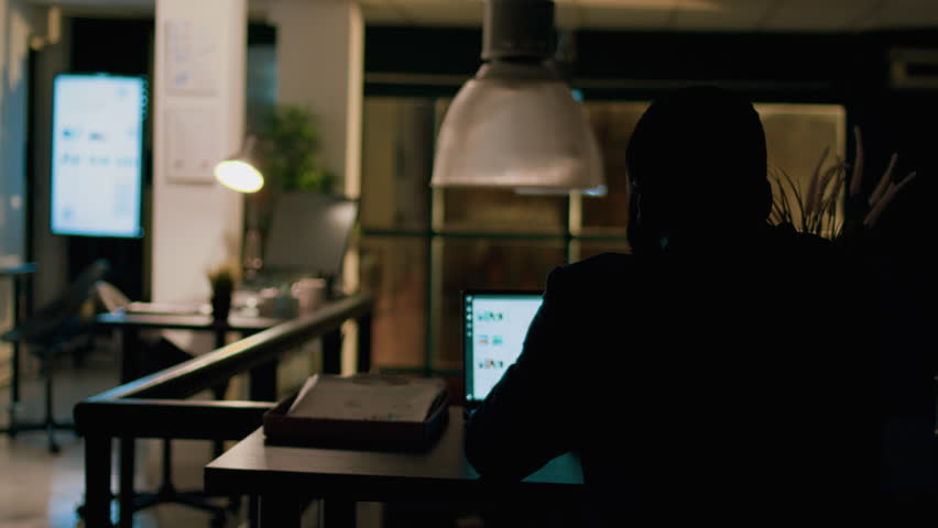 Employee left alone in the dark overnight in office, solving project tasks before next day deadline. Accountant working by himself in workspace, trying to keep up with paperwork Royalty-Free Stock Footage #1106690731