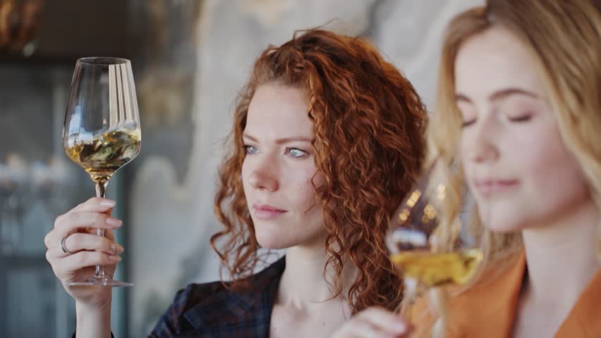 Beautiful women drinking tasting wine in restaurant. Wine expert holding glass of white wine. Slow motion video.