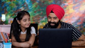 A Sikh Indian father-daughter watching an online video together on a laptop, online learning, online classes, digital education . A young tutor with her student learning online - Indian dad, school...