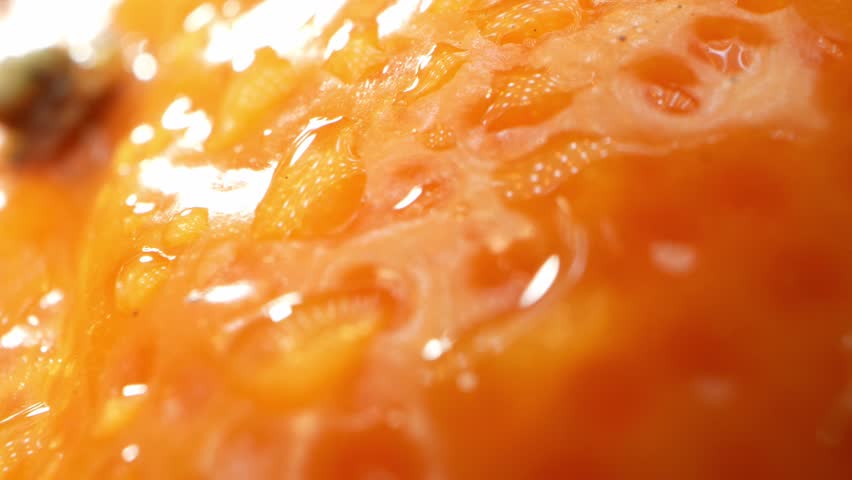 In a mesmerizing macro video, an orange glistens with droplets of water, each reflecting the world around it, creating a captivating play of light and color. Fruit concept. Orange background. 4K UHD
