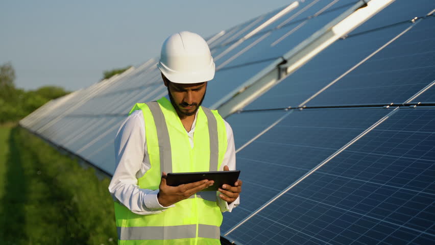 Young indian engineer working on tablet standing near solar panels with clear blue sky. Renewable green and clean energy. Copy space. Worker on job. Skill india Royalty-Free Stock Footage #1106701995