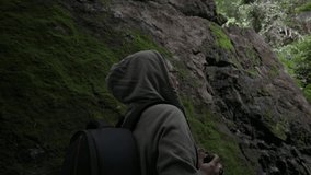 Female nature photographer taking picture with camera in the tropical rainforest while standing near the huge mossy rock. Solo woman hiker recording video the beautiful scenery in the wild. 
