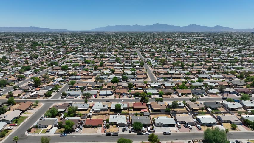 Sprawling suburb of city. Aerial truck shot over thousands of houses and homes in desert housing development. Middle class people commute into large USA city to work. Mountain range in background.