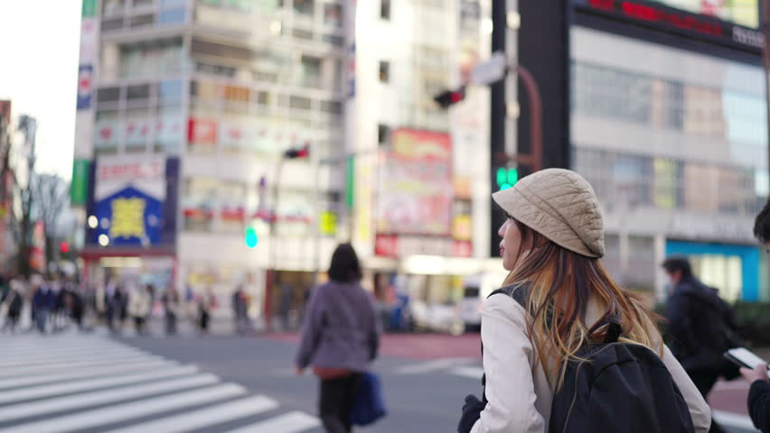 Young Asian woman walking on city street crosswalk and looking cityscape building in Tokyo, Japan. Attractive girl traveler enjoy urban outdoor lifestyle travel in Japan on winter holiday vacation. Royalty-Free Stock Footage #1106710149