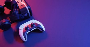 Video of close up of video game pad controller and vr headset with copy space on neon background. Video game, technology and global connections concept