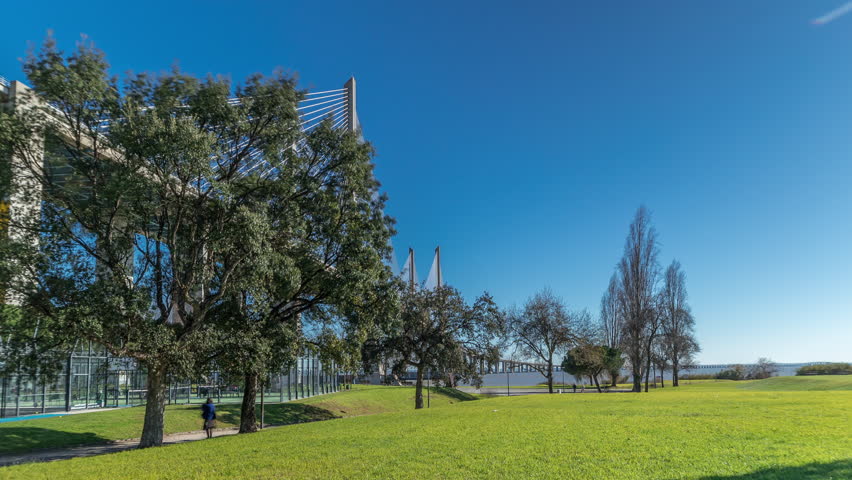 The Vasco da Gama Bridge timelapse hyperlapse viewed from green lawn with trees. Cable-stayed longest bridge flanked by viaducts and rangeviews that spans Tagus River in Park Nations. Lisbon, Portugal