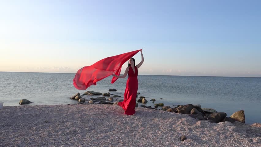 Beautiful free woman in red dress in wind on sea beach