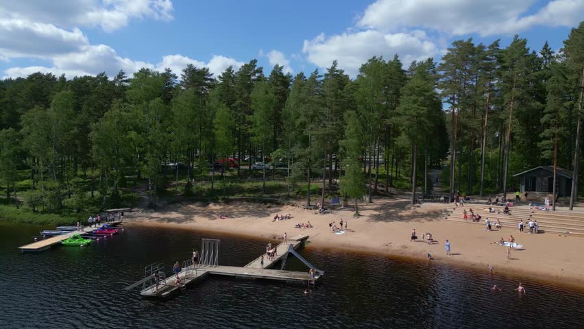 People play and jump off of dock swimming in alpine lake below forest in Sweden