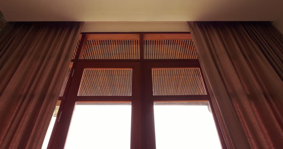 Heavy curtains closing automatically, low angle shot of top part of the window, looking from inside the room. Motorized curtain track installed in hidden curtain rod, ceiling edge is only visible